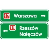 E-2b Drogowskaz tablicowy umieszczany nad jezdnią. Wskazuje na skrzyżowaniu lub bezpośrednio przed nim kierunki do miejscowości lub dzielnic miast